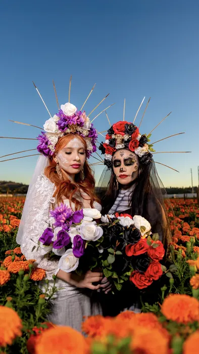 Two quinceañeras dressed as catrinas in a marigold field